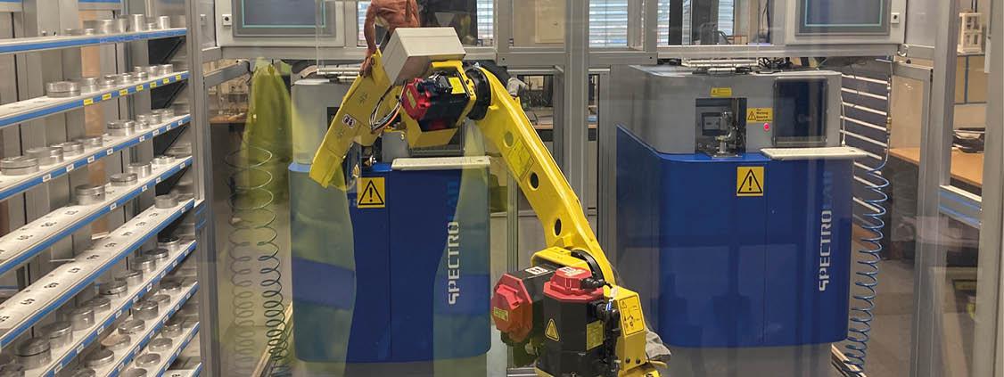 Yellow industrial robot working inside an automated production cell with enclosed machinery.